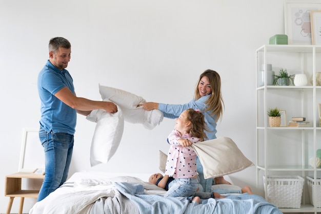 Vue latérale des membres de la famille se battre avec des oreillers