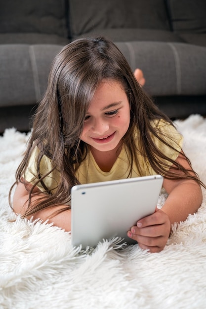 Adorable petite fille à l'aide d'une tablette numérique sur le sol à la maison