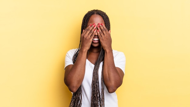 Afro black jolie femme souriante et se sentant heureuse, couvrant les yeux des deux mains et attendant une surprise incroyable