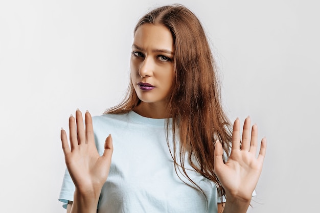 Arrêter. Suffisant. Une belle jeune fille tend la main vers la caméra pour arrêter l'effet. Femme avec du maquillage de mode avec des lèvres violettes sur fond gris isolé. Mauvais événements, désespoir et menace.