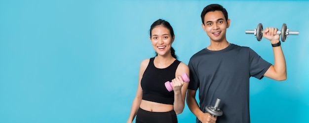 Photo asiatique belle femme heureuse tenant des haltères et debout avec son petit ami s'exerce isolé sur fond de couleur bleueconcept d'entraînement de fille mince et en bonne santé