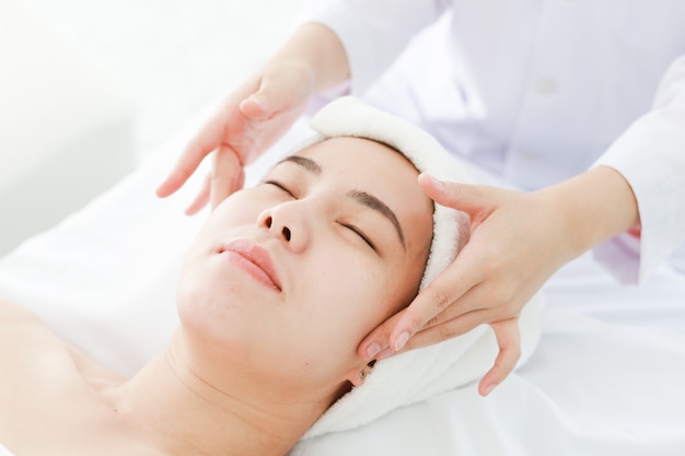 Asiatique jeune femme se cure thermale au salon de beauté. massage du visage au spa. traitement de beauté du visage