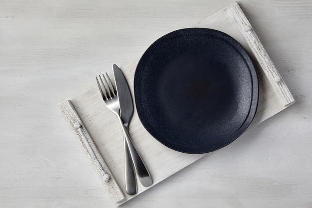 Une assiette en céramique sombre et un plateau de couverts sur une table en bois clair