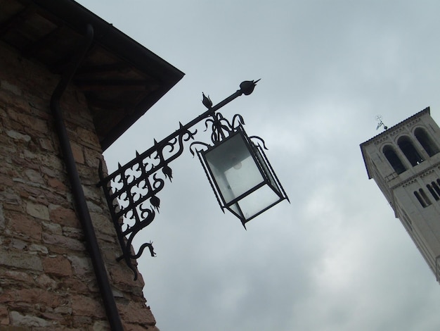 Assise Italie 1er décembre 2007 Photo prise sous un angle Vue de dessous d'une ancienne tour italienne et d'un beau lampadaire en métal Mur de briques d'un bâtiment avec une lanterne en forme de flèche