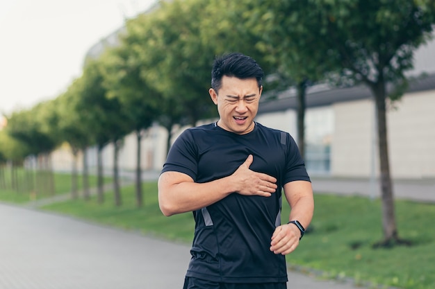 Photo athlète asiatique masculin, a des douleurs thoraciques dans le parc et en cours d'exécution, des douleurs cardiaques après un exercice cardio