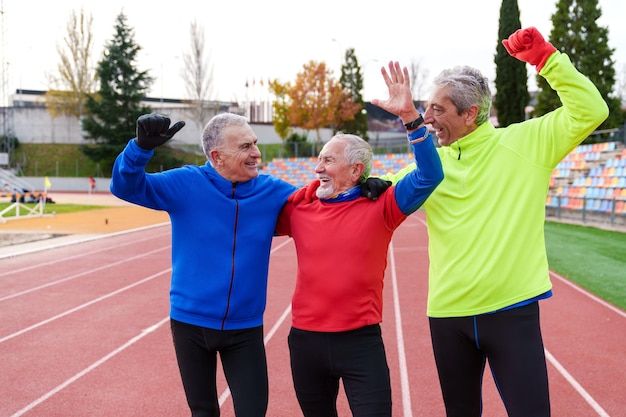 Photo des athlètes seniors heureux célèbrent leurs exploits en course à pied avec les mains levées et les sourires sur la piste