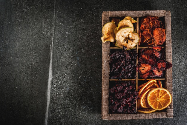 Baies et fruits séchés maison, récolte pour l'hiver: abricots, pommes, fraises, framboises, cerises, oranges. Dans la vieille boîte en bois, sur la vue de dessus de table en pierre noire