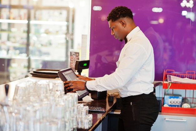 Photo un barman afro-américain porte un nœud papillon à l'aide d'un écran de terminal de paiement au bar