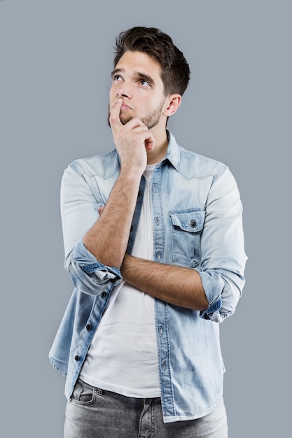 Beau jeune homme réfléchissant sur fond gris.