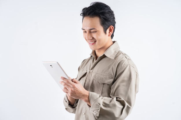 Beau jeune mécanicien en salopette à l'aide d'un ordinateur tablette pour travailler et sourire