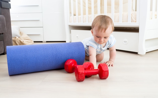 Photo bébé jouant au sol avec tapis de fitness et haltères. concept de sports pour enfants