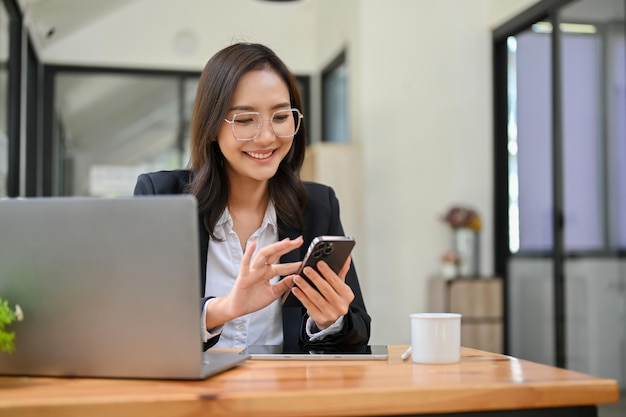 Belle femme d'affaires asiatique à l'aide de son smartphone à son bureau