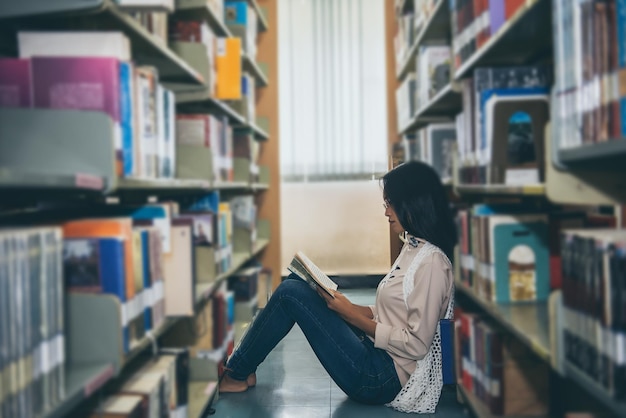 Belle femme asiatique porte des lunettes à la recherche d'un livre dans la bibliothèque