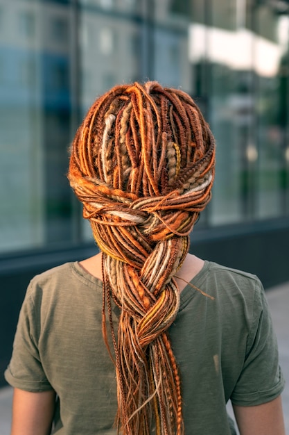 Photo belle fille avec une longue tresse de dreadlocks rouges. la fille se tient dos à la caméra. fermer.