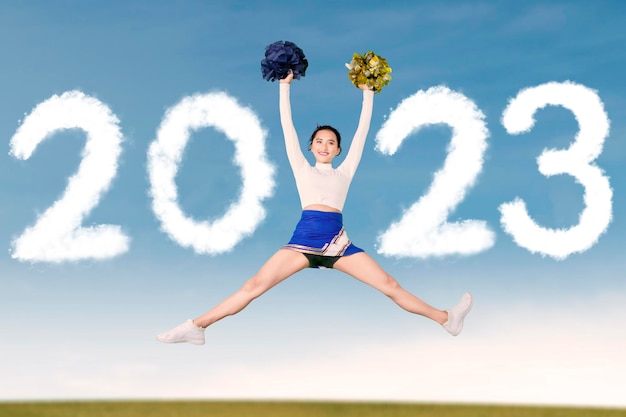 Belle fille de pom-pom girl sautant avec le numéro 2023