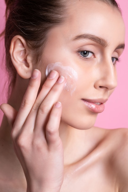 Belle jeune femme appliquant de la crème sur son visage rose