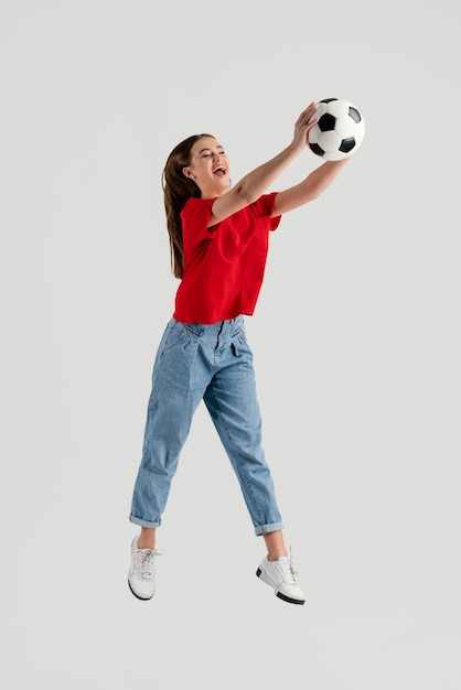 Belle jeune femme avec ballon de football sautant