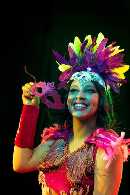 Belle jeune femme en masque de carnaval et costume de mascarade dans des lumières colorées