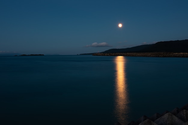 Belle pleine lune se levant derrière la montagne se reflétant dans la mer au crépuscule. L'île d'Iriomote.