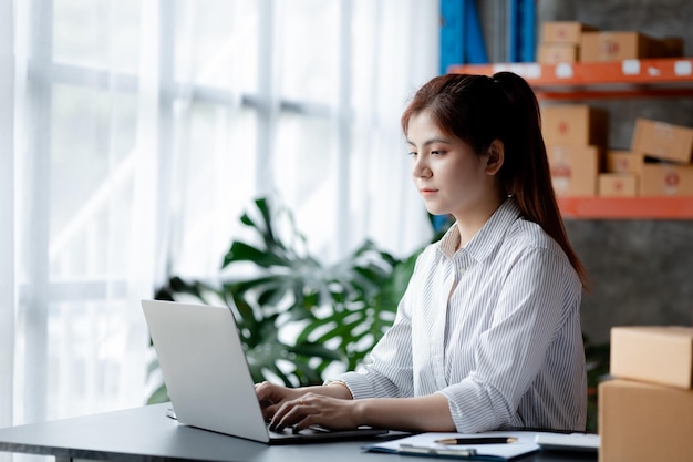 Une belle propriétaire d'entreprise asiatique ouvre une boutique en ligne, elle vérifie les commandes des clients qui envoient des marchandises via une entreprise de messagerie concept d'une femme ouvrant une entreprise en ligne