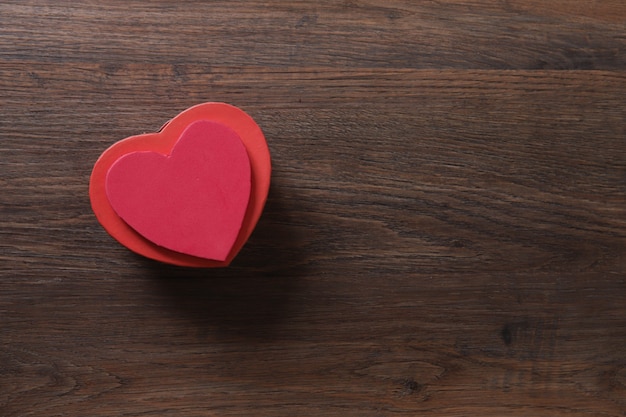 Boîte cadeau en forme de coeur rouge sur table en bois.