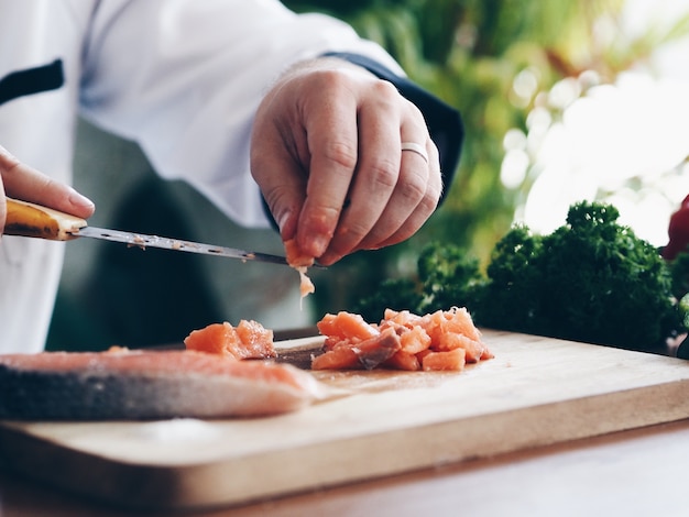 Bouchent les mains de chef couper le saumon frais sur la planche à découper.