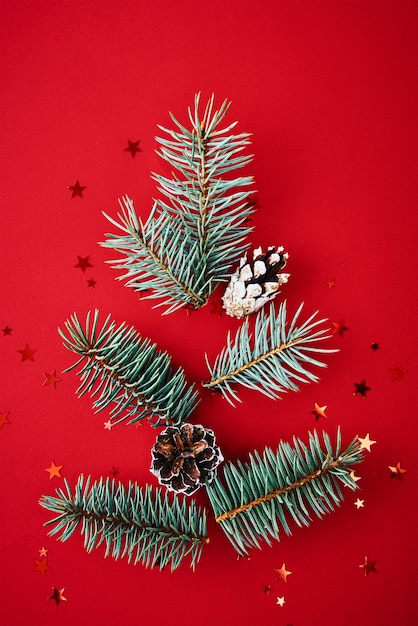 Branches de sapin en forme de sapin de Noël avec des confettis festifs sur fond rouge