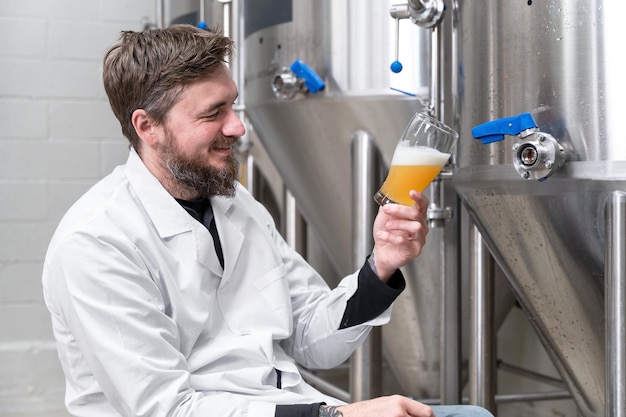 Brasseur portant une blouse blanche contrôlant le processus de fermentation de la bière tout en travaillant dans une usine de bière moderne