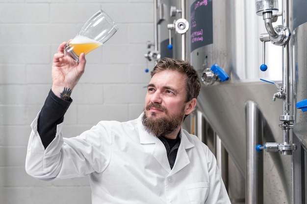 Brasseur portant une blouse blanche contrôlant le processus de fermentation de la bière tout en travaillant dans une usine de bière moderne