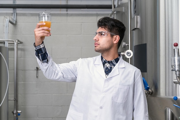 Brasseur portant une blouse blanche contrôlant le processus de fermentation de la bière tout en travaillant dans une usine de bière moderne