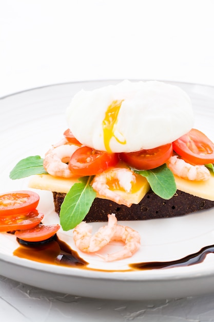 Bruschetta appétissante sur pain de seigle avec oeuf poché, tomate, crevettes et roquette sur une assiette