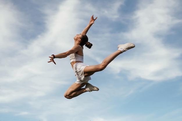 Photo le ciel bleu avec des nuages qui sautent une jeune femme en forme est à l'extérieur