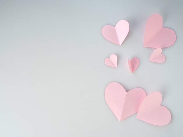 Coeurs de papier rose placés sur fond blanc.