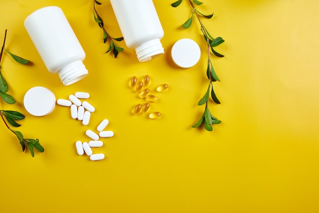 Composition de pilules, huile de poisson, vitamines avec feuilles vertes sur surface jaune