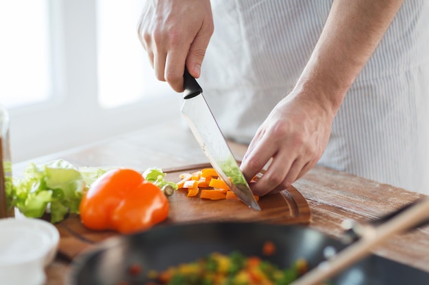 concept de cuisine, de nourriture et de maison - gros plan d'une main masculine coupant du poivre sur une planche à découper à la maison