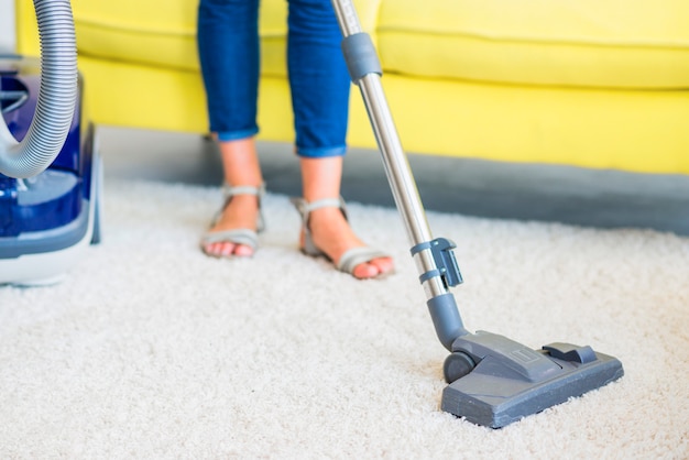 Photo coupe basse d'un concierge nettoyant un tapis avec un aspirateur