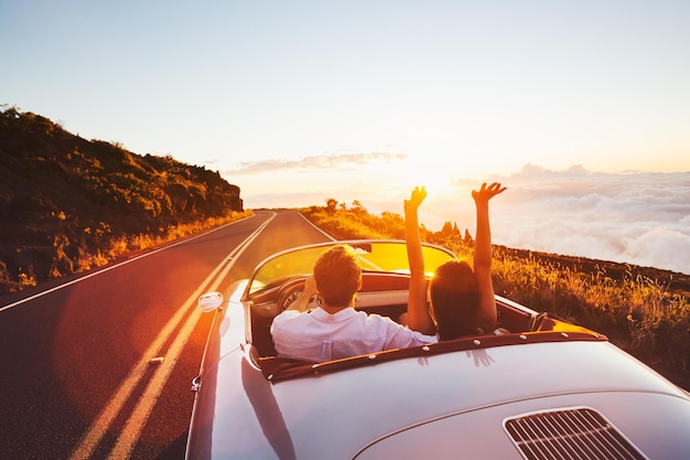 Photo un couple heureux conduisant sur une route de campagne vers le coucher du soleil dans une voiture de sport vintage classique