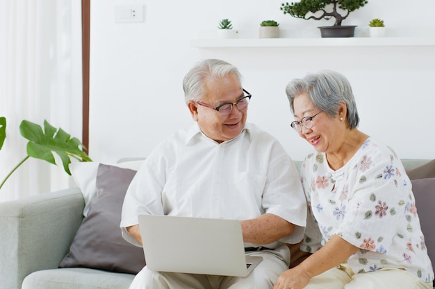 Photo couple de personnes âgées asiatiques utilisant un ordinateur portable pour effectuer des recherches sur internet, faire des achats en ligne et acheter une assurance dans le salon à la maison senior avec concept technologique