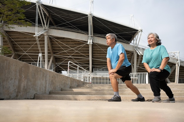 Photo les couples seniors asiatiques portent des vêtements de sport et réchauffent les muscles avant de faire de l'exercice à l'extérieur le matin.