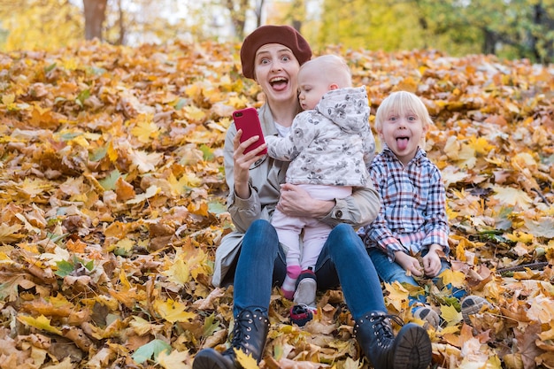 Drôle jeune mère et deux enfants assis dans les feuilles d'automne dans le parc