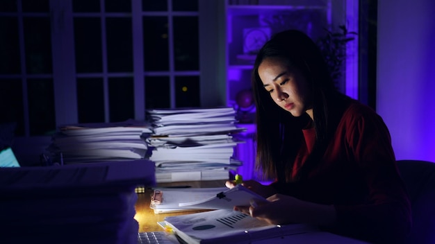 Femme d'affaires asiatique travaillant dur tard avec beaucoup de documents à la maison. Occupé et épuisé par les heures supplémentaires de travail la nuit.