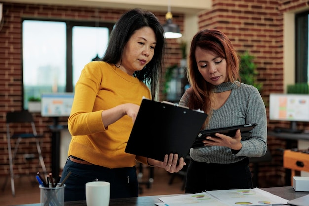 Femme d'affaires debout à côté d'un pigiste regardant des papiers avec des graphiques marketing analysant des statistiques travaillant à la stratégie de l'entreprise lors d'une réunion d'affaires au bureau de démarrage. Lieu de travail moderne