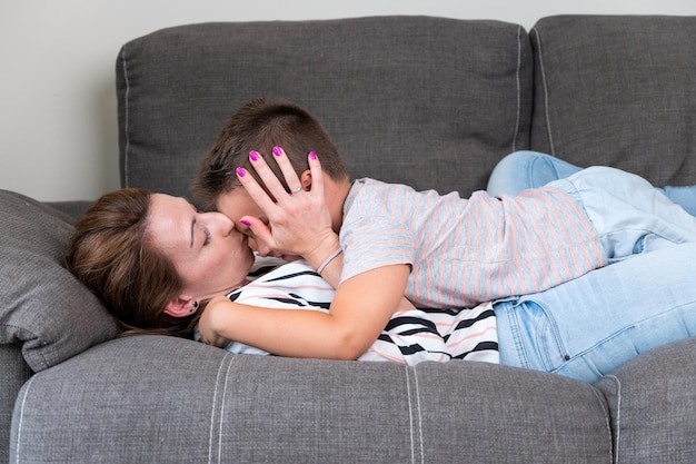 Femme allongée sur un canapé embrassant son petit fils dans la joue Maman avec petit garçon passant joyeusement du temps dans un salon confortable à la maison