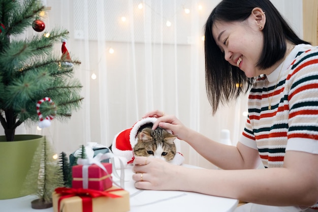 Photo une femme asiatique décore un arbre de noël et habille son chat avec un thème de noël.