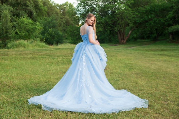 Femme aux cheveux blonds vêtue d'une belle robe bleue à manches longues en plein air