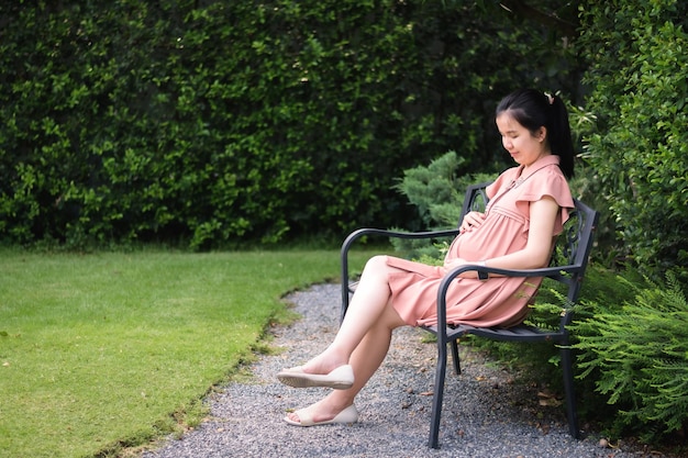 Femme enceinte tenant son ventre lorsqu'elle est assise sur un banc dans le jardin