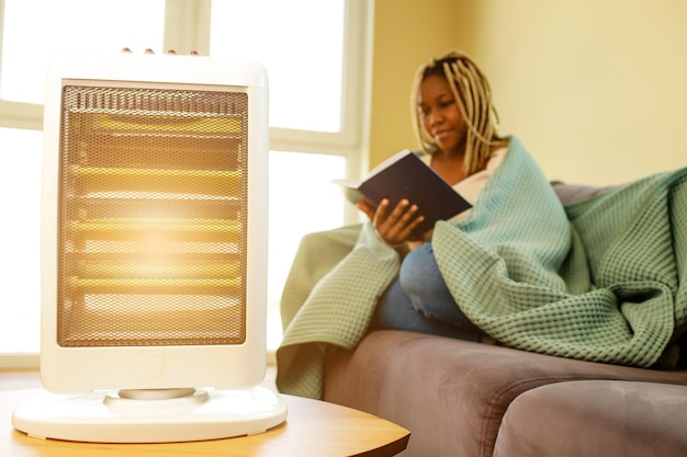 Femme latino-américaine avec couverture lisant un livre dans une chambre froide avec chauffage