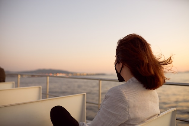 Photo femme avec masque et lunettes de soleil sur un bateau de banlieue au coucher du soleil.