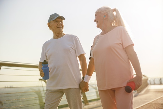 Photo femme mature sportive et homme marche main dans la main le long du pont au coucher du soleil