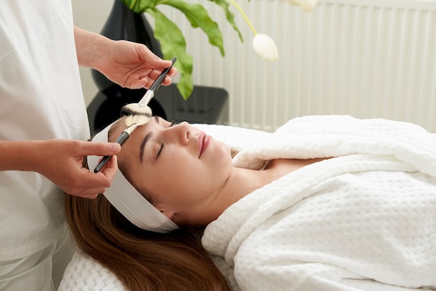 Photo une femme reçoit un traitement de brosses à la clinique de beauté. concept de soins de la peau du visage. détente dans un salon spa